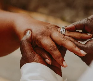 A close up of two hands with a person is sliding a wedding ring on another's person finger.