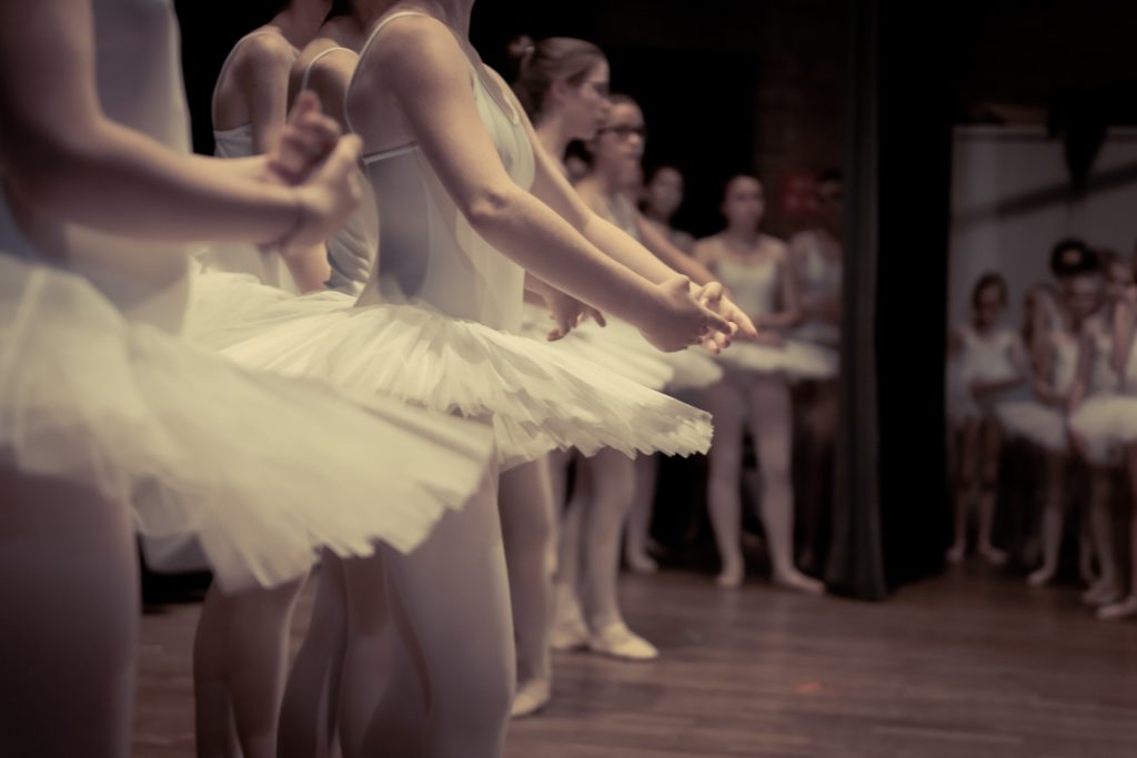 A ballet class is taking place with students wearing white tutus.